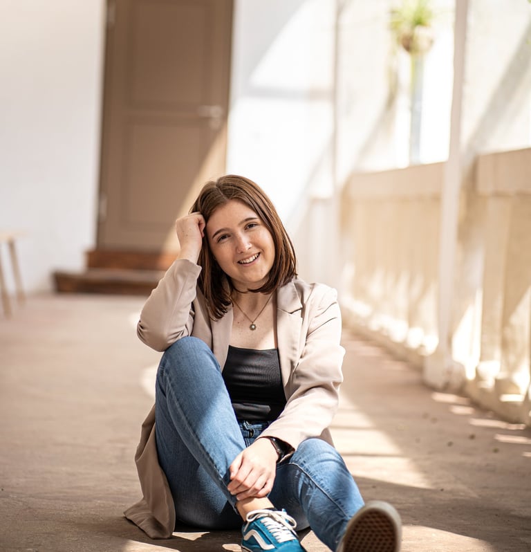 Frau sitzt am Boden in einer lockeren Position und schaut nett in die Kamera