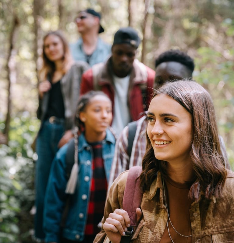 Group of friends hiking together through a forest, one woman smiling in the foreground