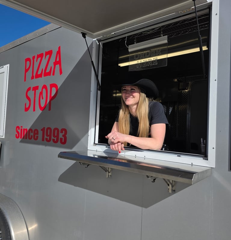 a girl wearing a cowboy hat smiling from the window of a grey pizza truck