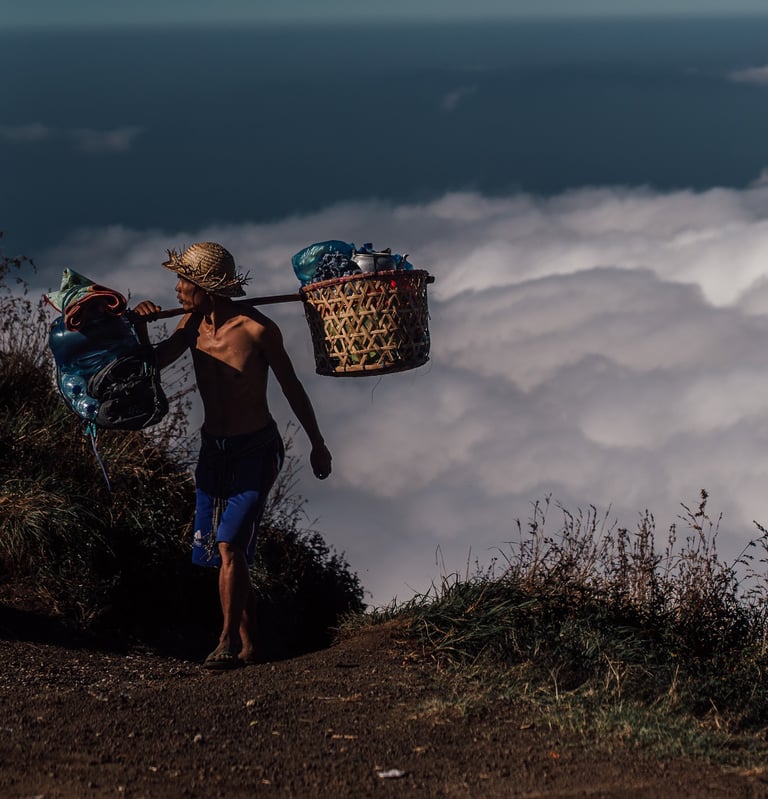 a porter walking up rinjani mountain with food and tant on his back