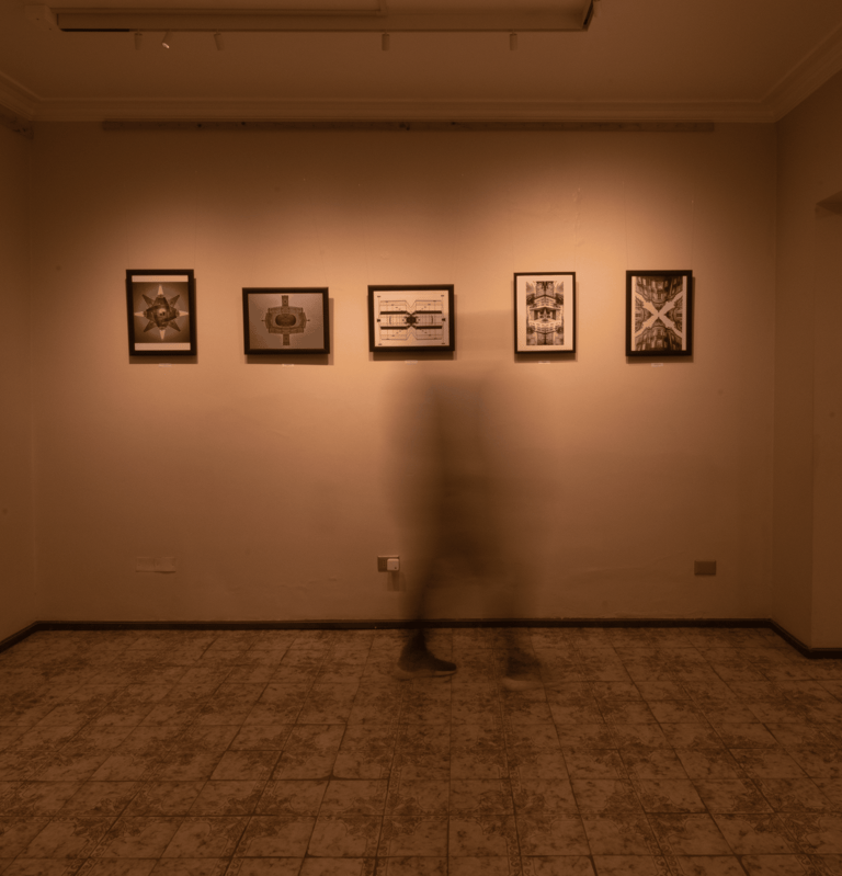 Una persona parada en una habitación con cuadros en la pared. Iluminacion calida