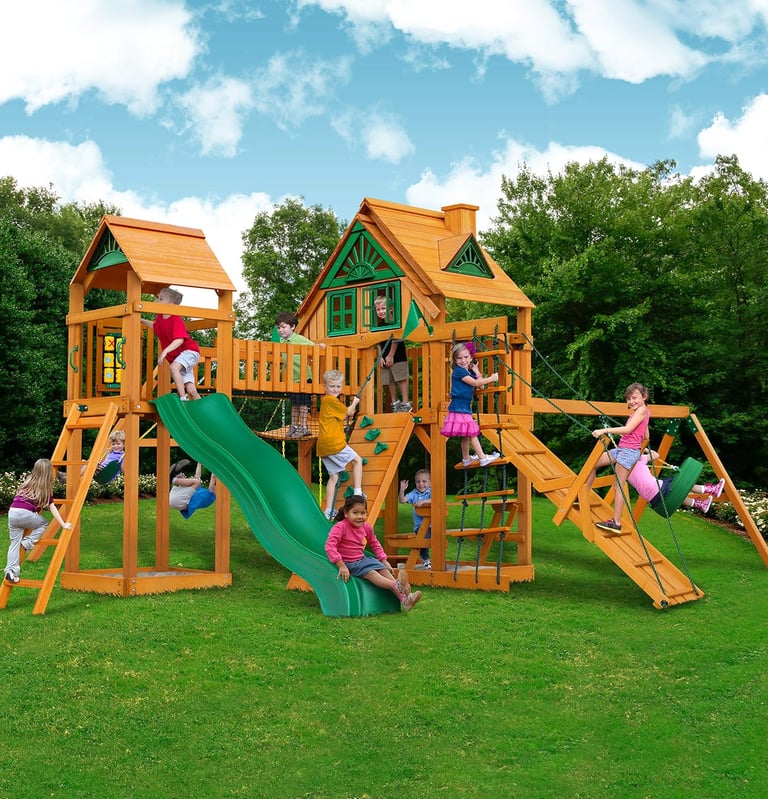 Children playing on a large cedar wood backyard swing set with a slide and playhouse.