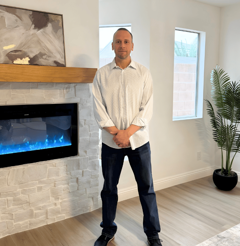 Professional man standing in a modern living room next to a white stone fireplace with blue flames.