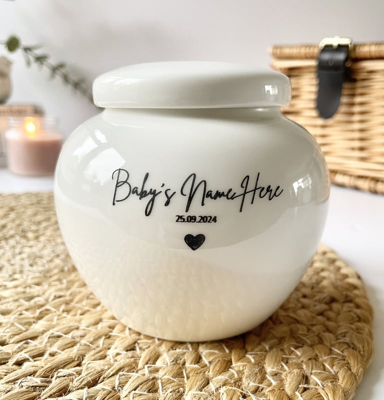 Rounded white ceramic urn with glossy finish, black script text “Baby’s Name Here 25.09.2024” and a 