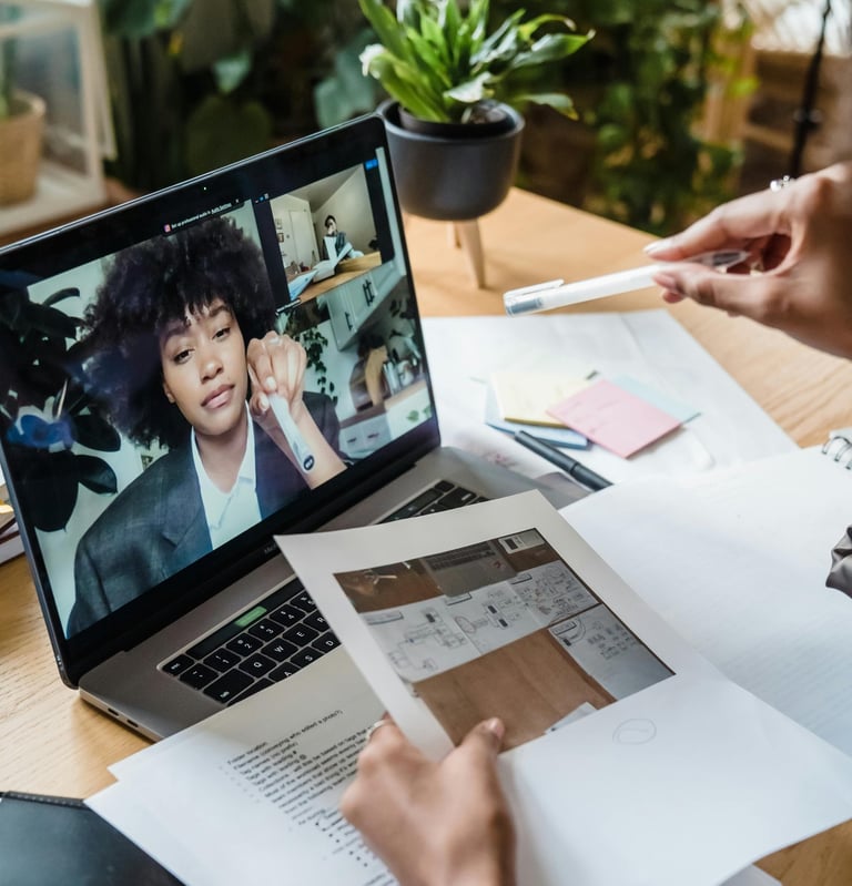 Professional architect reviewing floor plans during a remote video conference on a laptop.