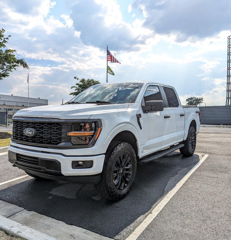 A white Ford F-150 Lariat pickup truck with black wheels parked in an asphalt lot under a cloudy sky.