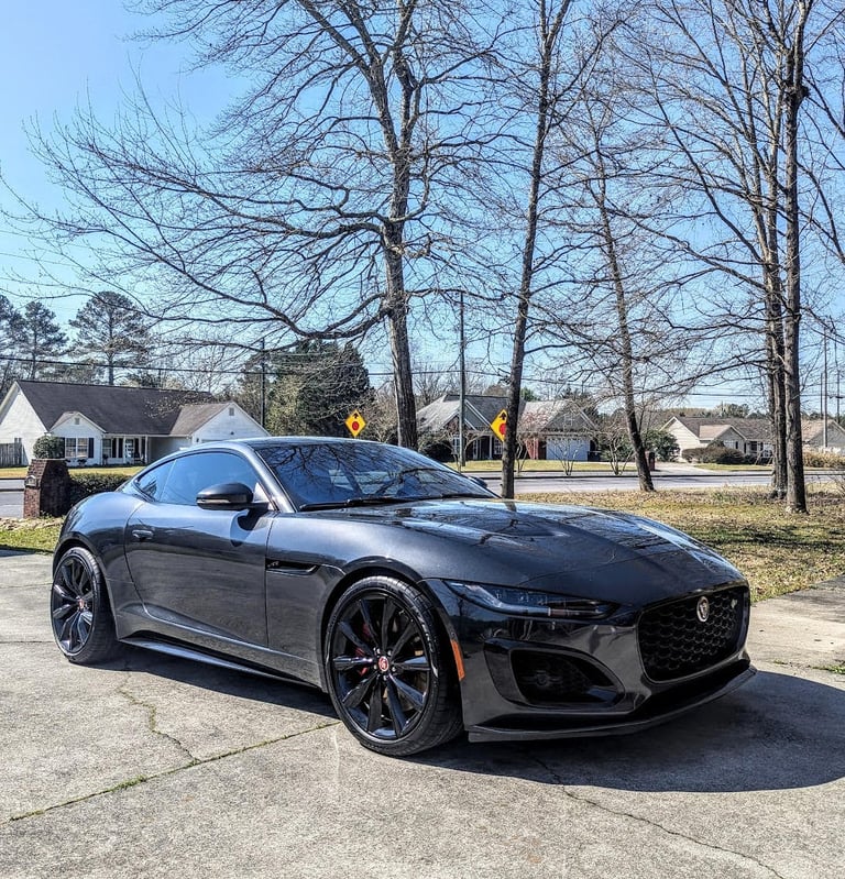 Dark grey Jaguar F-Type luxury sports car parked on a sunny driveway with black wheels.