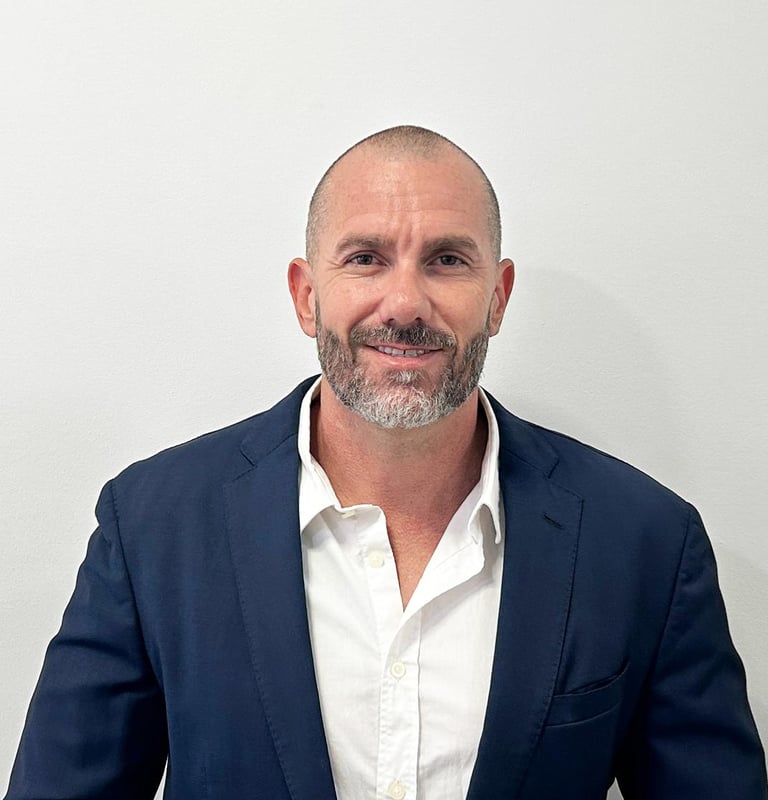 Professional portrait of a smiling businessman with a beard wearing a navy blue suit and white shirt.