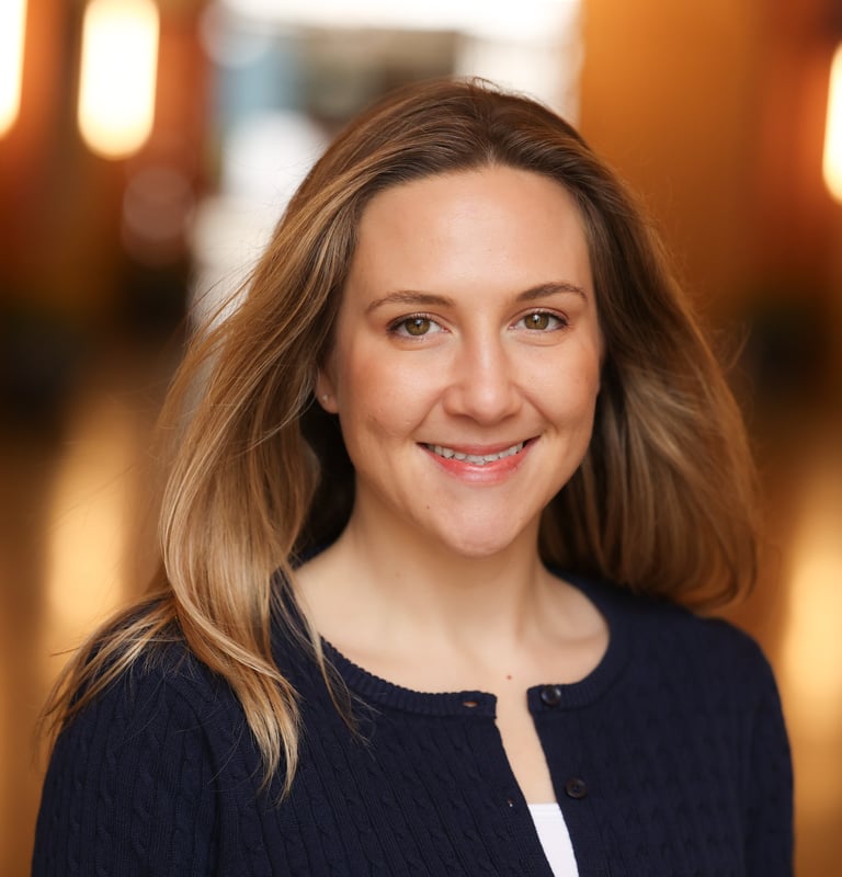 Professional headshot of a smiling woman with blonde hair in a navy blue cardigan.