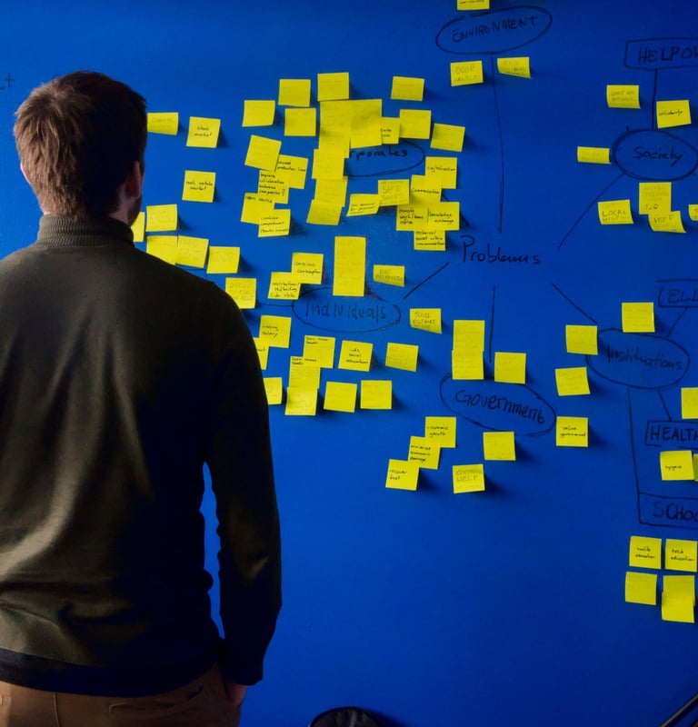 A man brainstorms using yellow sticky notes on a blue wall for project planning and problem-solving.