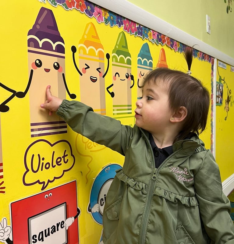 a young child is pointing at a wall with a crayon FANTASTICLANDLEARNING CENTER