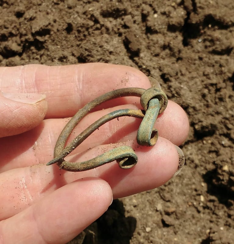A bronze, circular Iron Age brooch held in the hand of the finder.