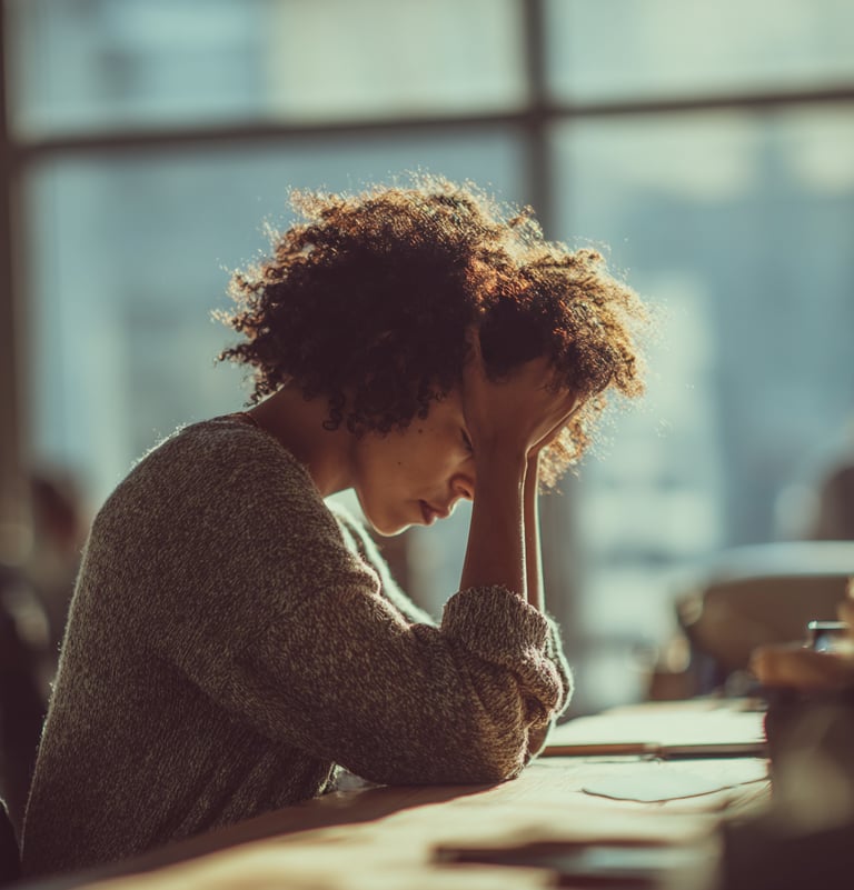 femme empathe assise à son bureau et qui se tient la tête entre les mains tellement elle est fatigué