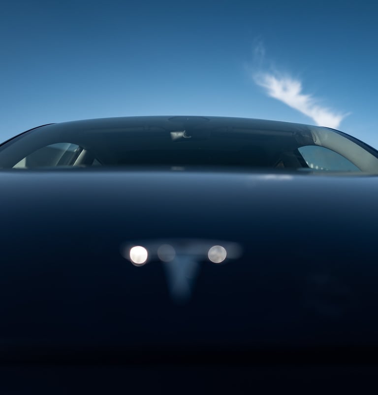 Low‑angle front view of an electric car’s hood TESLA and windshield under a blue sky, By ACAT Photos