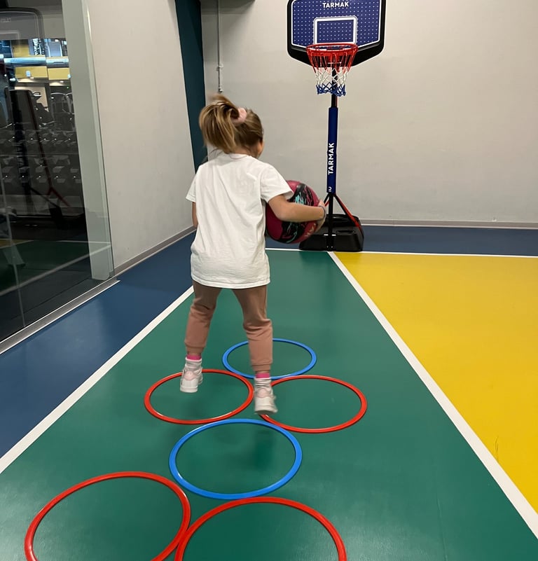 Bambina che gioca con un pallone su un campo multisport nella palestra Move 2 Grow a Milano, utilizzando cerchi colorati