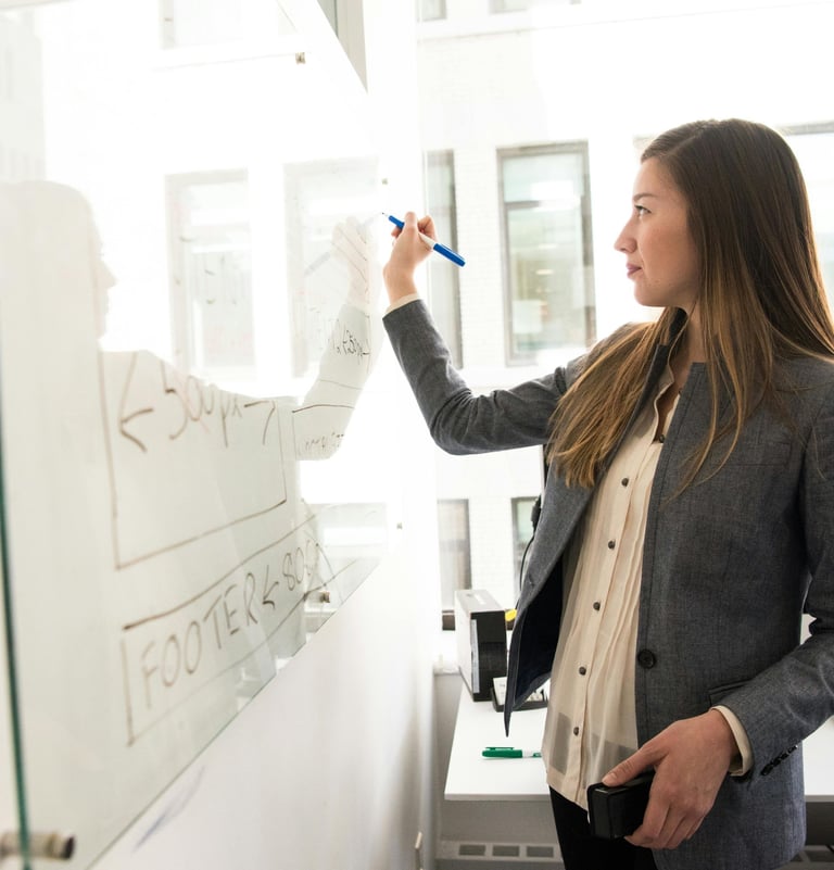 A business professional woman writing website wireframe plans on a glass whiteboard in a bright office.