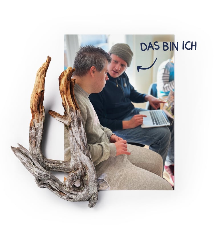 Mann mit Laptop erklärt einem jungen Mann mit Down-Syndrom etwas