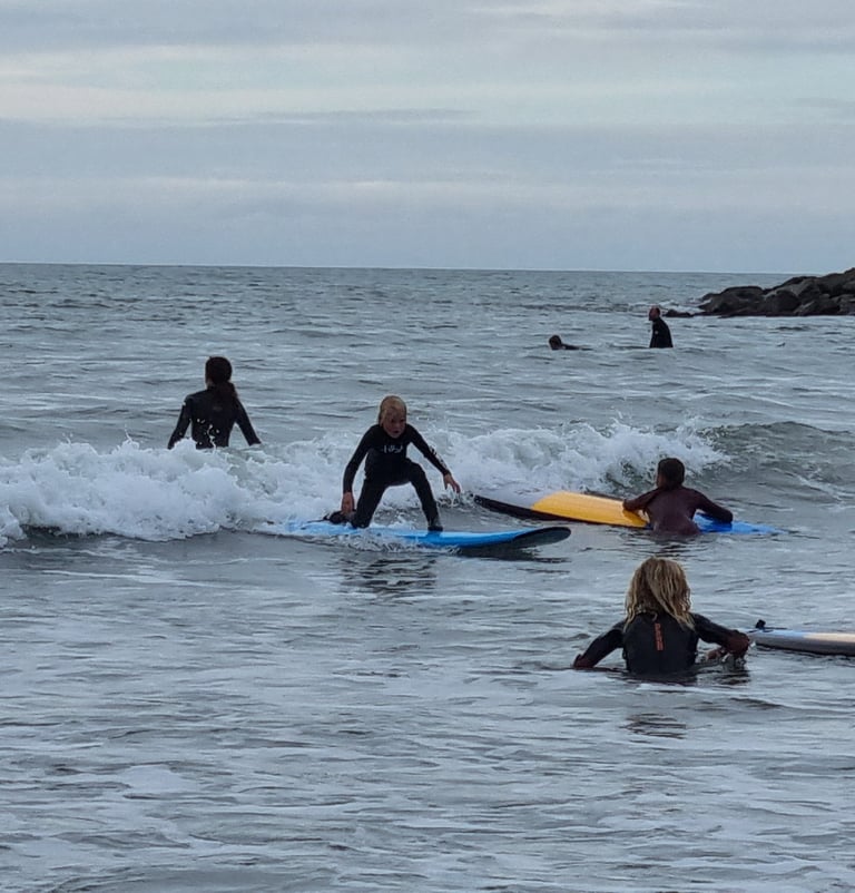 A busy after school surf club lesson with a young male surfer an a wave other children watching