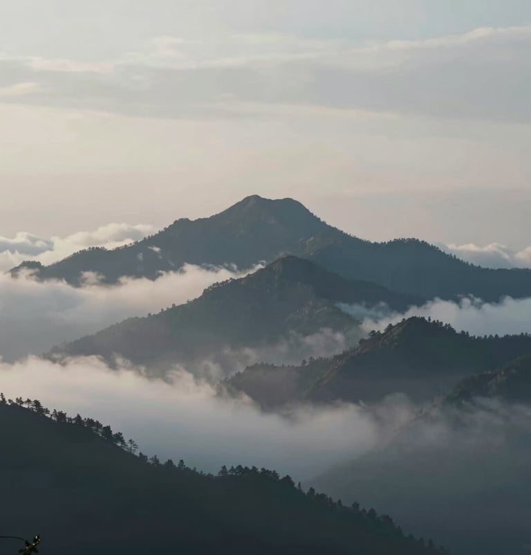 A cinematic landscape shot of a mountain peak piercing through a layer of low clouds, early morning light, muted #A0B0C0 tones and deep blue shadows, vast and epic composition, 4K film quality.