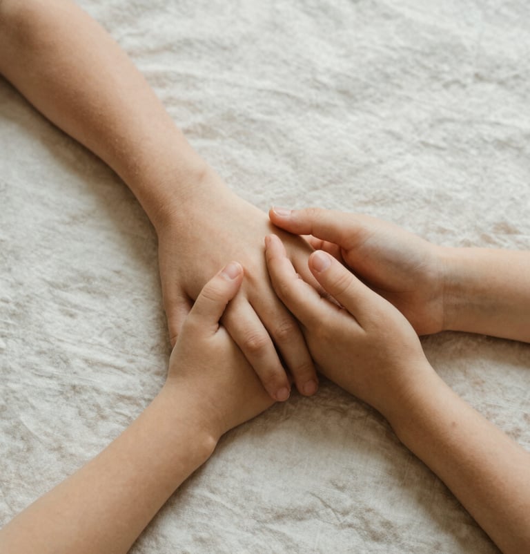 An artistic detail shot of a parent and child's hands intertwining, set against a soft off-white linen background. The lighting is warm and natural, creating a sense of intimacy and grace. North American style.