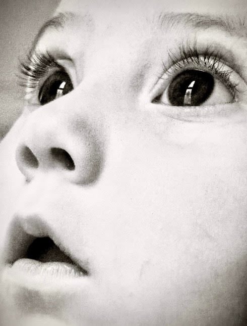 Black and white close-up of a baby girl's face, looking upward with wide eyes, capturing a sense of wonder and innocence