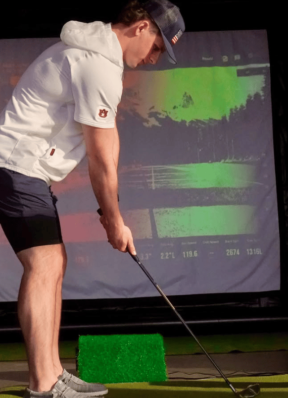 A male golfer practicing his swing on an indoor golf simulator with performance data tracking.