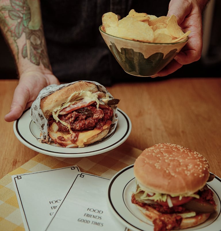 Dan holding a Winnipeg Fat Boy style burger and chips over a table.