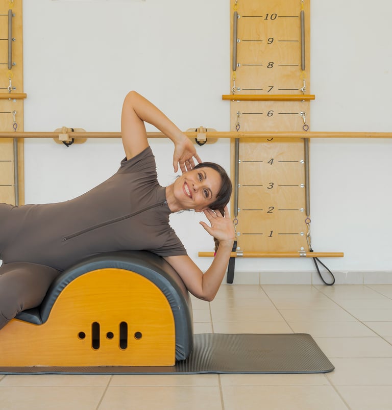 Woman smiling while performing a side bend exercise on a Pilates Spine Corrector barrel.