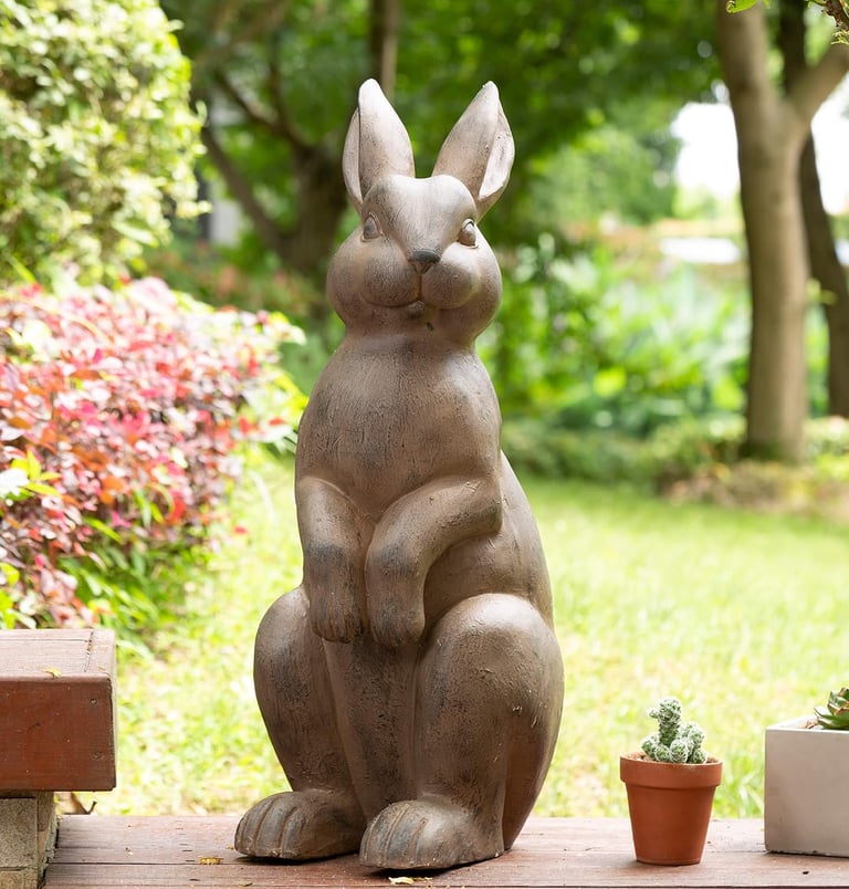 Decorative stone rabbit statue standing in a lush green garden setting.