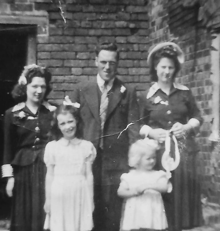 Vintage black and white portrait of a family of five posing in front of a brick wall.