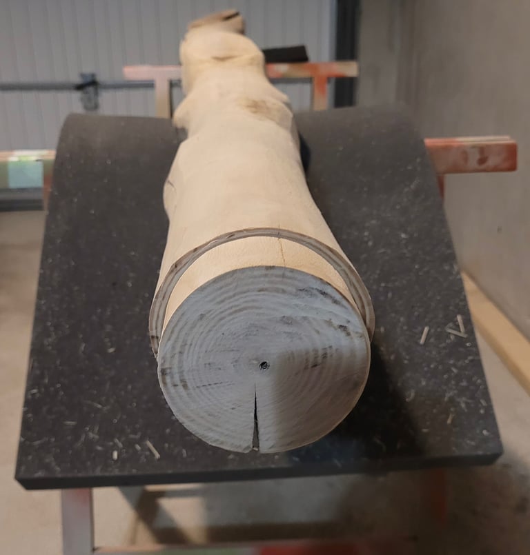 A debarked light wood log being prepared for a woodworking project on a workshop bench.