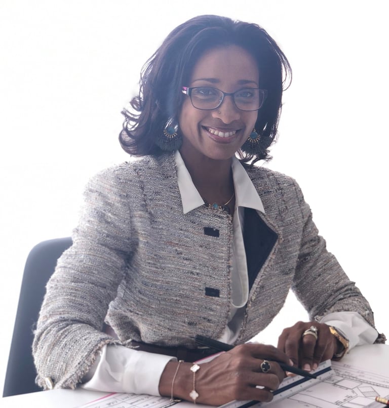 Smiling professional female architect in a blazer working on blueprints at her office desk.