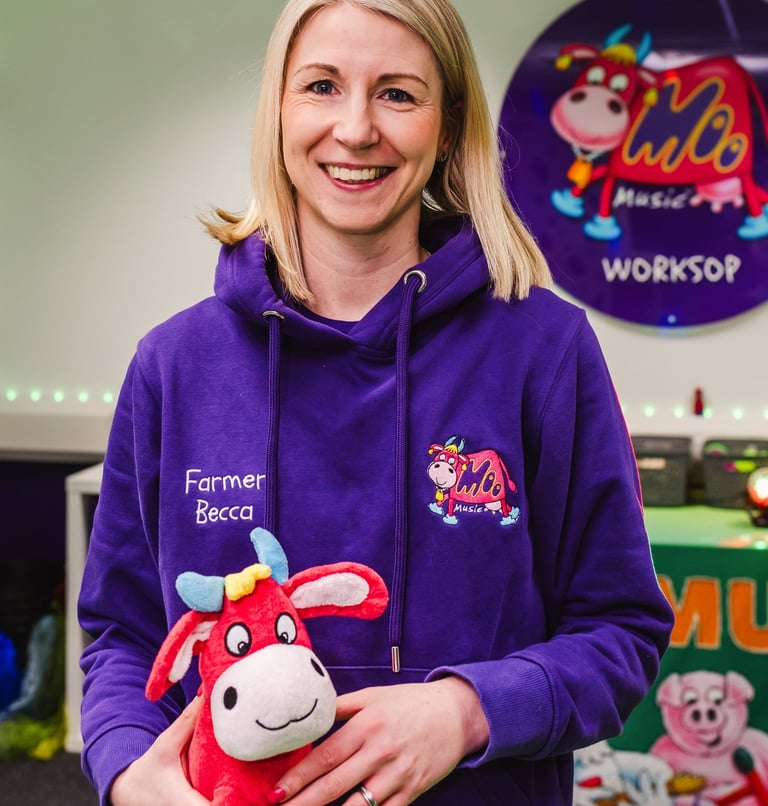 Farmer Becca stood in the Moo Room smiling, holding Maggie Moo in her branded purple Moo hoodie.