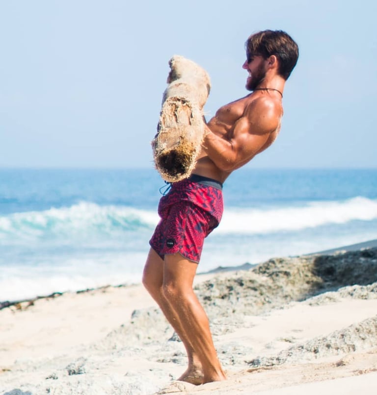 a strong man lifting a log on a beach 