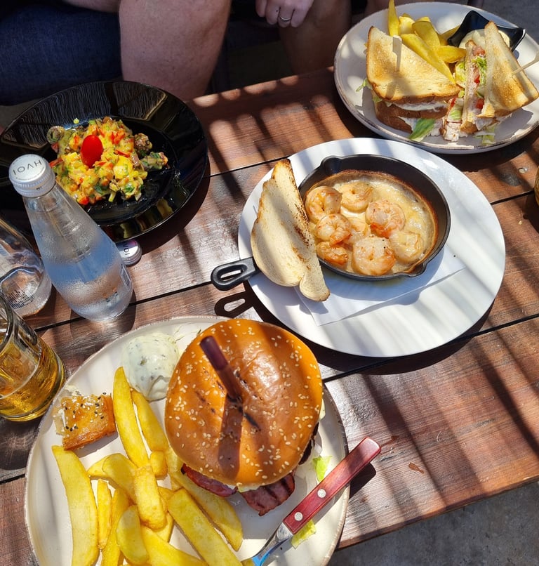 Gourmet lunch spread featuring a cheeseburger with fries, garlic shrimp in a skillet, and a club sandwich.