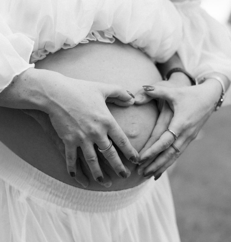 Detall de la panxa d'una dona embarassada formant un cor amb les mans en una sessió de maternitat 
