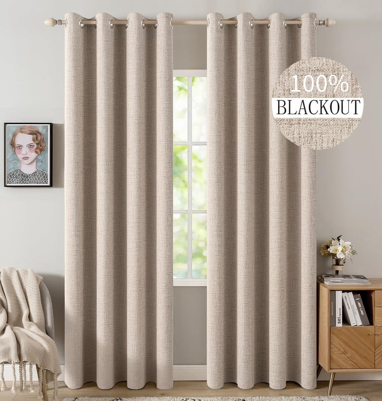 Pair of beige textured 100% blackout curtains hanging on a wooden rod in a modern living room.