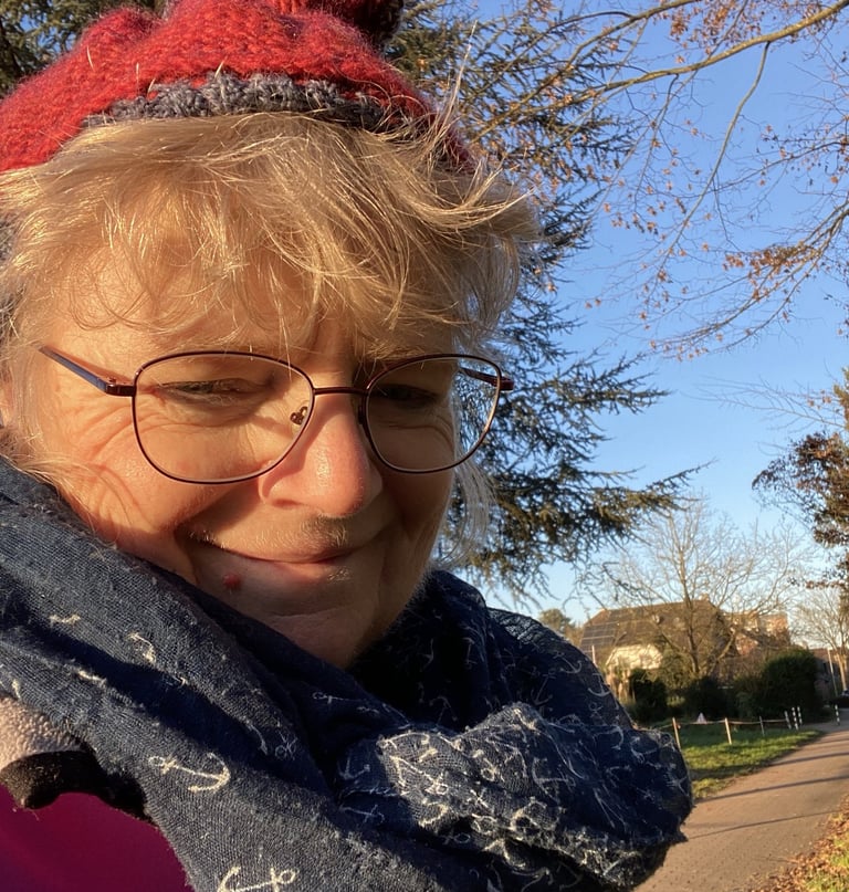 Person mit roter Mütze, Brille und dunkelblauem Schal mit Anker-Muster im Freien an einem sonnigen T