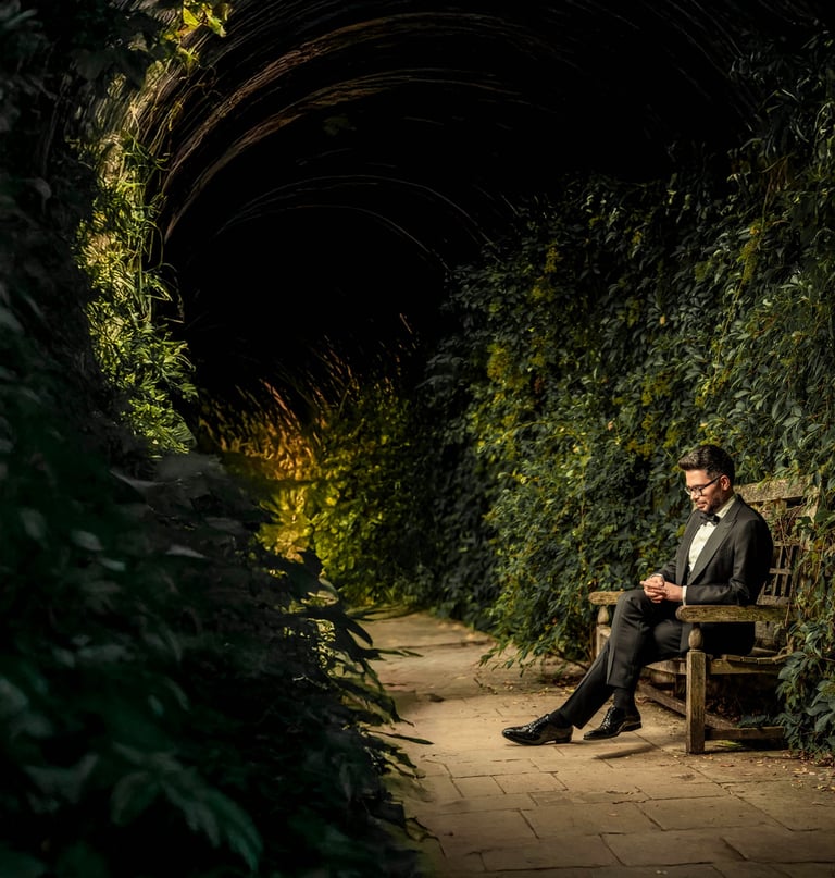Groom sitting on a wooden bench in a vine-covered tunnel, captured by Fred Art Studio.