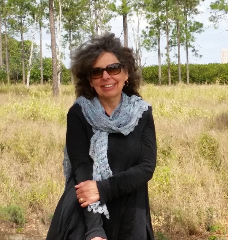 Photo of Linda Nickel in a field wearing a hand-woven scarf.