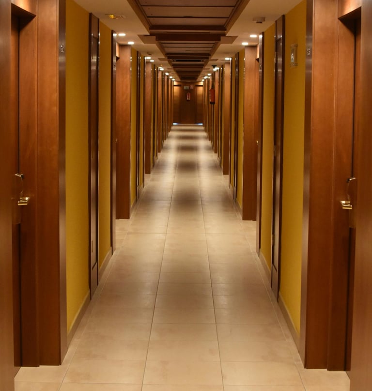 Long, narrow hotel hallway with symmetrical wooden doors, yellow walls, and warm ceiling lighting.