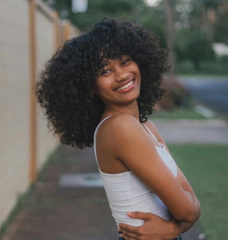Smiling Black woman with curly hair standing outdoors, symbolizing joy and self-worth.