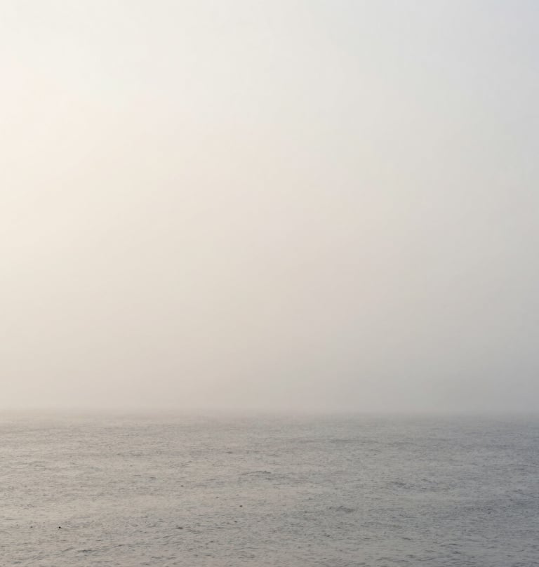 A full-width landscape photograph of a misty, minimalist horizon in Northern Europe. The sea and sky blend into a seamless field of soft light gray and off-white. Tranquil, ethereal, and deeply focused on atmospheric texture.