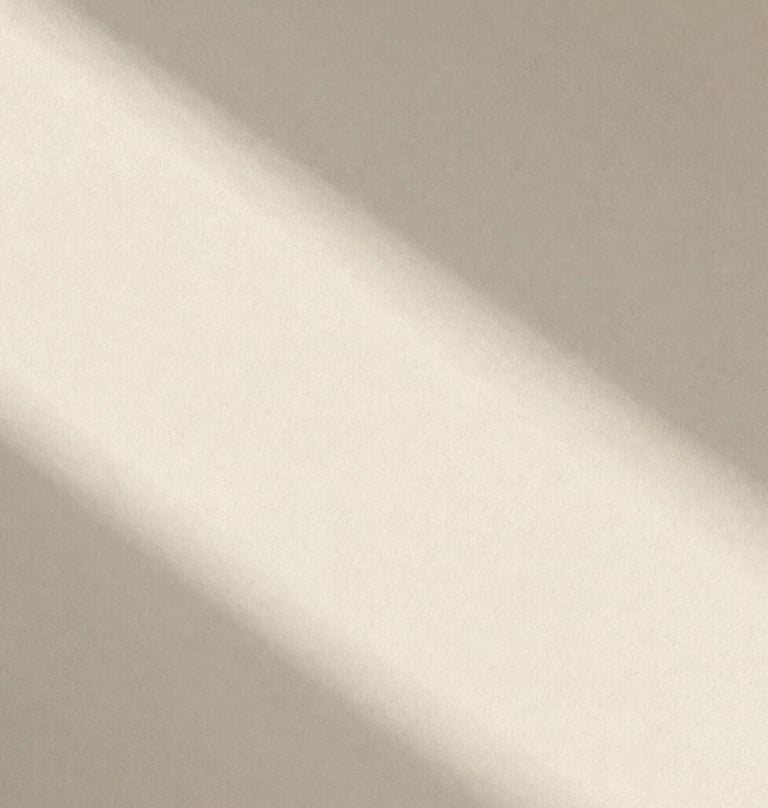Large, grainy, underexposed photo of a morning shadow falling across a textured wall. The light is soft and hazy. Editorial zine style, very minimal, emphasizing whitespace and the brand's cream palette (#F8F3EC).
