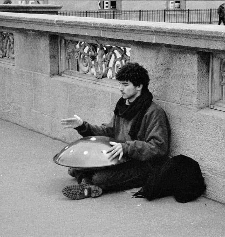 a man sitting on the sidewalk playing the handpan instrument.