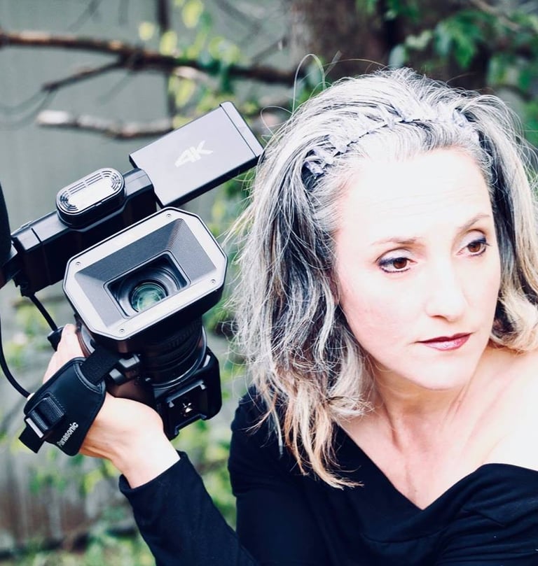 Micheline Brulotte filme avec une caméra professionnelle dans un décor extérieur naturel.