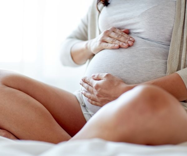 a pregnant woman holding her belly while sitting on a bed