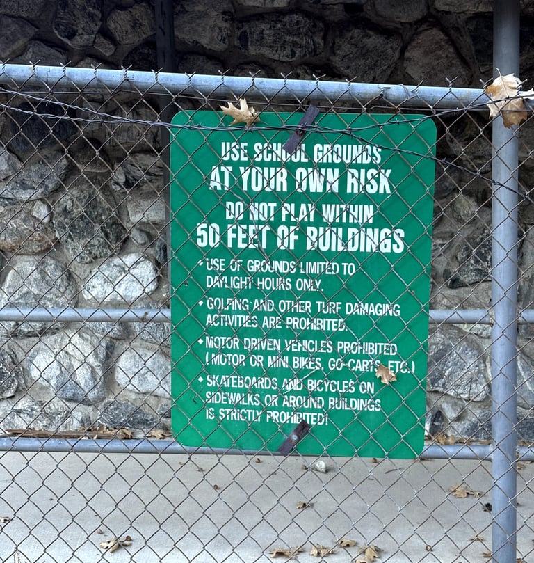 Green “Use School Grounds at Your Own Risk” sign on fence at Fallsvale Schoolhouse.