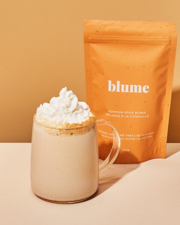 A cup of pumpkin spice latte with whip cream on top along with the orange bag of pumpkin spice latte mix beside it.