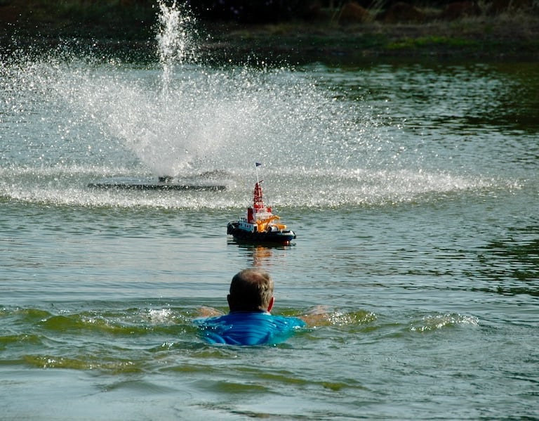 Man swimming in lake toward model tugboat